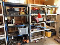Three plastic utility shelving units in a garage filled with various items, contents not included.
