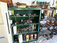 Green metal shelves filled with automotive parts, containers of fluids, adhesives, and metal hand tools.