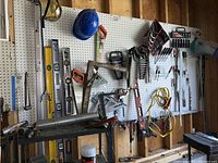 Garage pegboard with various hand tools such as wrenches, squares, and jumper cables