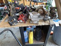 Overview of workshop vises and clamps on wooden bench with jack stands and fluid containers underneath