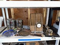 Shelf showing two tall stainless steel canisters, several wicker organizers including one with Waterford Crystal clock, metal coin bank, ashtray, and round pan with rust. Barometer/thermometer not fully visible but present.
