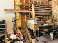 Wide view showing stacked wood and plywood sheets, some stored vertically, in a garage with insulation on walls and other construction materials nearby.