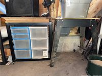 Photo showing two metal workbenches side by side. One bench has a six-drawer blue and clear plastic storage unit underneath. Both have wooden tops and black metal legs.