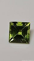 Square cut apple green peridot gemstone with brilliant facets and clear transparency.