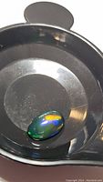 Oval cabochon Ethiopian black opal with bright rainbow flash on black background surface, showing colors of blue, green, yellow, and red.