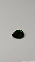 Pear cut chrome diopside gemstone seen from a distance showing its vibrant electric green color and teardrop shape.