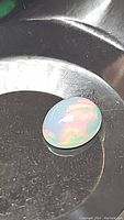Oval cabochon opal laid on dark surface showing pink, red, green, yellow rolling flash colors with translucent body.