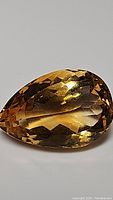 Close-up image of a pear-shaped golden citrine gemstone showing facets and color saturation.
