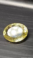 Close-up photo showing the oval faceted lemon citrine gemstone flat on a dark surface, bright yellow color with internal reflections visible