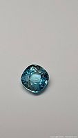 Photo showing cushion cut natural blue zircon gemstone with deep ocean blue color on neutral background.