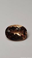 Close-up front view of a large oval imperial topaz gemstone showing peach undertone and faceted cut