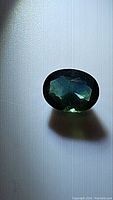 Oval cut sapphire gemstone with deep forest green and blue undertones seen against a white background from the top view.