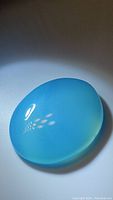 Smooth, polished natural icy blue chalcedony gemstone pendant with oval cabochon cut reflecting light.