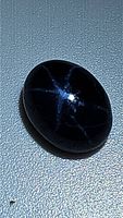 Oval cabochon blue star sapphire showing 6-ray star effect under light