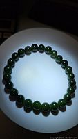 Photo showing the round green jade bead bracelet laid flat in a circular shape under lighting that highlights the beads' natural color and polish.