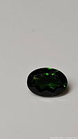 Close-up image of a faceted oval green chrome diopside gemstone on white background showing color and cut details.