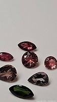 Seven natural fancy cut and colored tourmaline gemstones in assorted cuts and colors displayed on white background.
