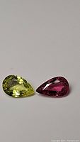 Two pear cut natural tourmalines, one yellow-green and one pink-purple, on a plain background showing clarity and color.