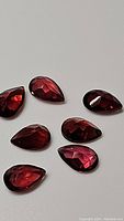 Seven pear-shaped cherry red garnet stones arranged with facets visible, showing their color and clarity.