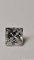 Top-down image of a clear, square princess cut moissanite gemstone showing intricate faceting and brilliance.