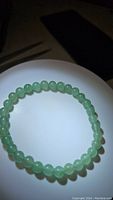 Photo showing full view of the green aventurine bead bracelet coiled on a white surface under light.