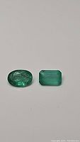 Oval and rectangular cut green emerald stones shown on neutral background, highlighting clarity and cut.