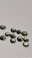 Close-up image showing 12 small round mint green sapphire cabochons arranged on a plain white surface.