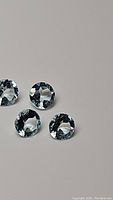 Four round-cut clear sky blue topaz gemstones with faceted surfaces on a light gray background
