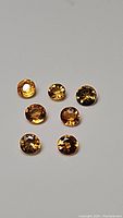 Photo showing seven round cut natural sapphires in sunshine yellow-orange color range, arranged on a flat surface.