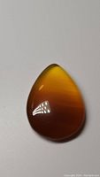 Front view of polished pear-shaped yellow onyx cabochon showing color gradient and glossy surface under neutral lighting.