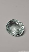 Photo of oval cut untreated aquamarine gemstone showing faceted top side with light reflections and internal inclusions.