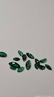 Thirteen natural green marquis cut Zambian emerald gemstones arranged on a white background under normal lighting.