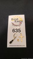 All jewelry items displayed on a Rest Easy Auctions and Removals numbered card 635: cross pendant, stud earrings, leverback earring with black drop, and earring back.