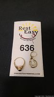 Two 16kt gold jewelry pieces: one earring with red stone and one broken ring on a Rest Easy Auctions card
