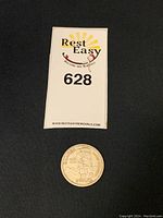 Canadian silver dollar coin on black background with auction card number 628 visible.