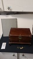 Photo showing hardwood jewelry box with brass lock and key on table next to the blue and white Asian fabric covered book.