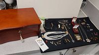 Full view of wooden jewelry box next to assortment of costume jewelry spread on black cloth
