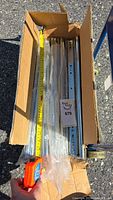 Box with multiple metal drawer slides measured with tape measure showing 20-inch length, partially wrapped in plastic