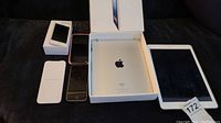 Lot contents showing 1 white iPad, 3 iPhones including one in box, one in rose gold case, and one black phone.