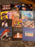 Photo showing a collection of approx. 12 vinyl records with album covers arranged on floor; includes K-Tel Power House, Van McCoy, Dire Straits, The Isley Brothers, Joan Armatrading among others.