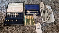 Full lot showing boxed silver-plated spoons with ivory-like handles, boxed gold-plated Community by Oneida spoons, and assorted forks and spoons in white container.