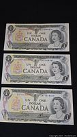Three 1973 Canadian 1 dollar bills displayed face up, showing Queen Elizabeth II and denomination with serial numbers visible.
