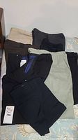 Photo showing eight pairs of folded dress pants in various colors including black, khaki, brown, gray and navy on bedspread.