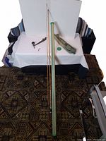 Full length bamboo fishing rod alongside carrying tube and hand tool with fishing lure on white tablecloth.