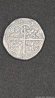 Close-up of one side of the silver coin showing a cross-like design with aged markings and symbols.