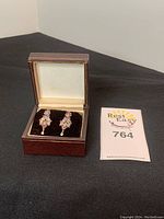 Closed view of earrings in a brown jewelry box beside a card with lot number