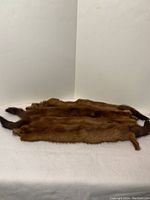 Three natural brown mink fur pelts laid flat showing fur and tails