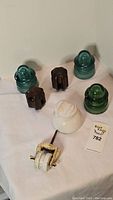 Full view showing all seven insulators on white background. Includes green glass, brown ceramic, white ceramic, and ceramic pulley insulators.