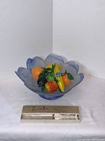 Blue frosted glass fruit bowl with wavy edges and leaf pattern with artificial fruit inside, shown alongside the glass cutting tool in box.