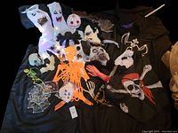 Full view of assorted Halloween masks, flags, skeleton decorations, socks with faces, and more spread on black fabric.